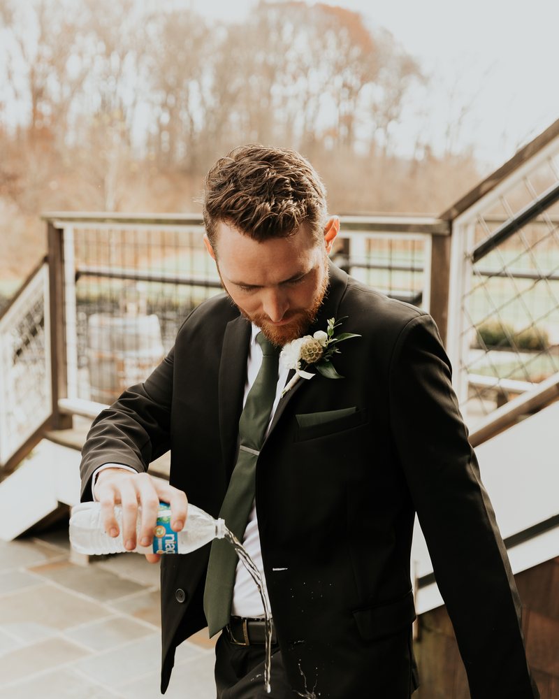 A groom pouring a water bottle onto his sleeve at his wedding