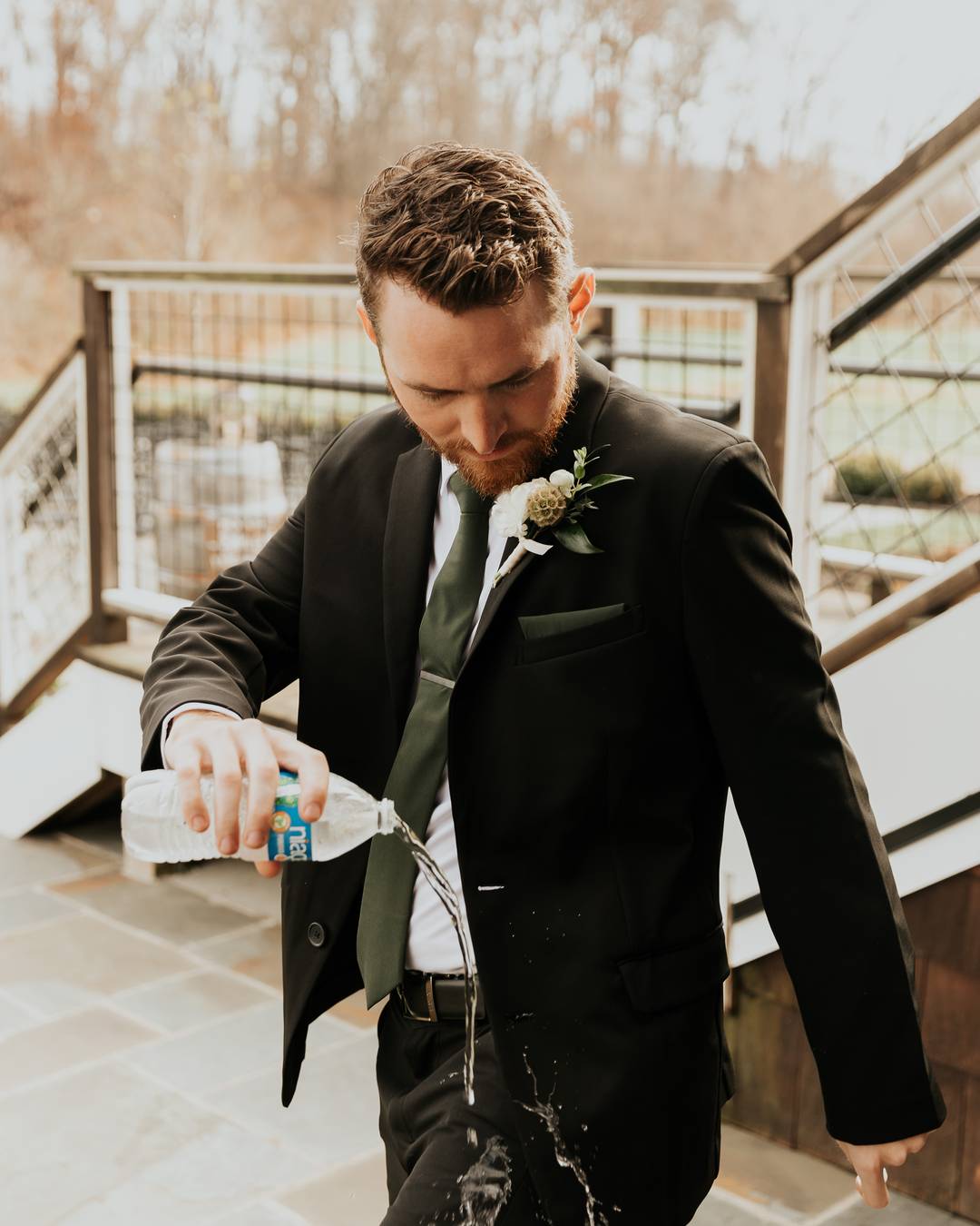 A groom in a suit pouring a water bottle onto his own shirt sleeve at his wedding